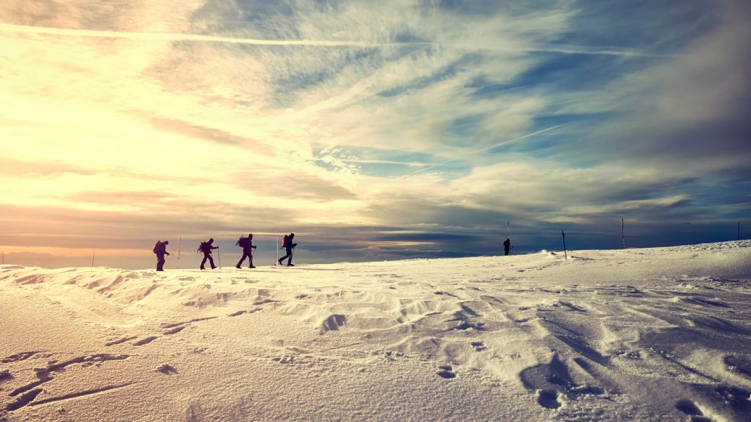 Winter landscape with travelers silhouettes at sunset.